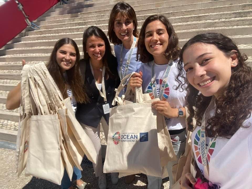 Rita stands in the centre of 4 young women holding ocean conference bags, to her left is Carolina Mendorca, the others are young volunteers from the conference venue. All are smiling and looking straight to camera.